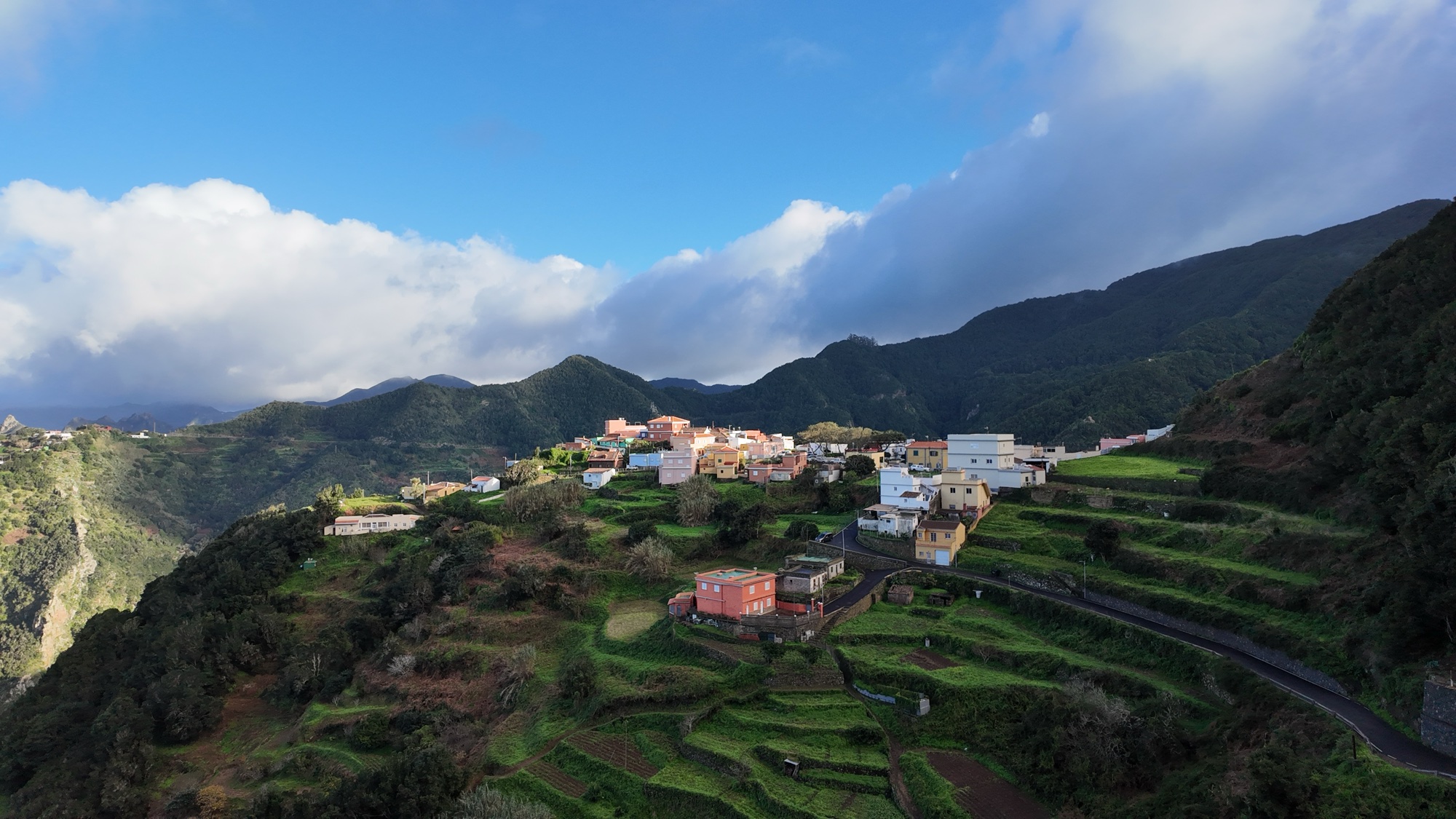 A village on green terraced ridges in the Anaga mountains, cloud pouring over the laurel forest behind