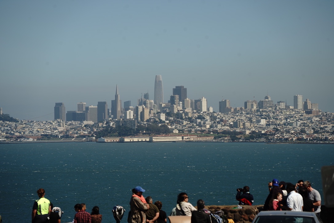 The San Francisco skyline across a choppy bay, with a crowd of people along the shore watching it