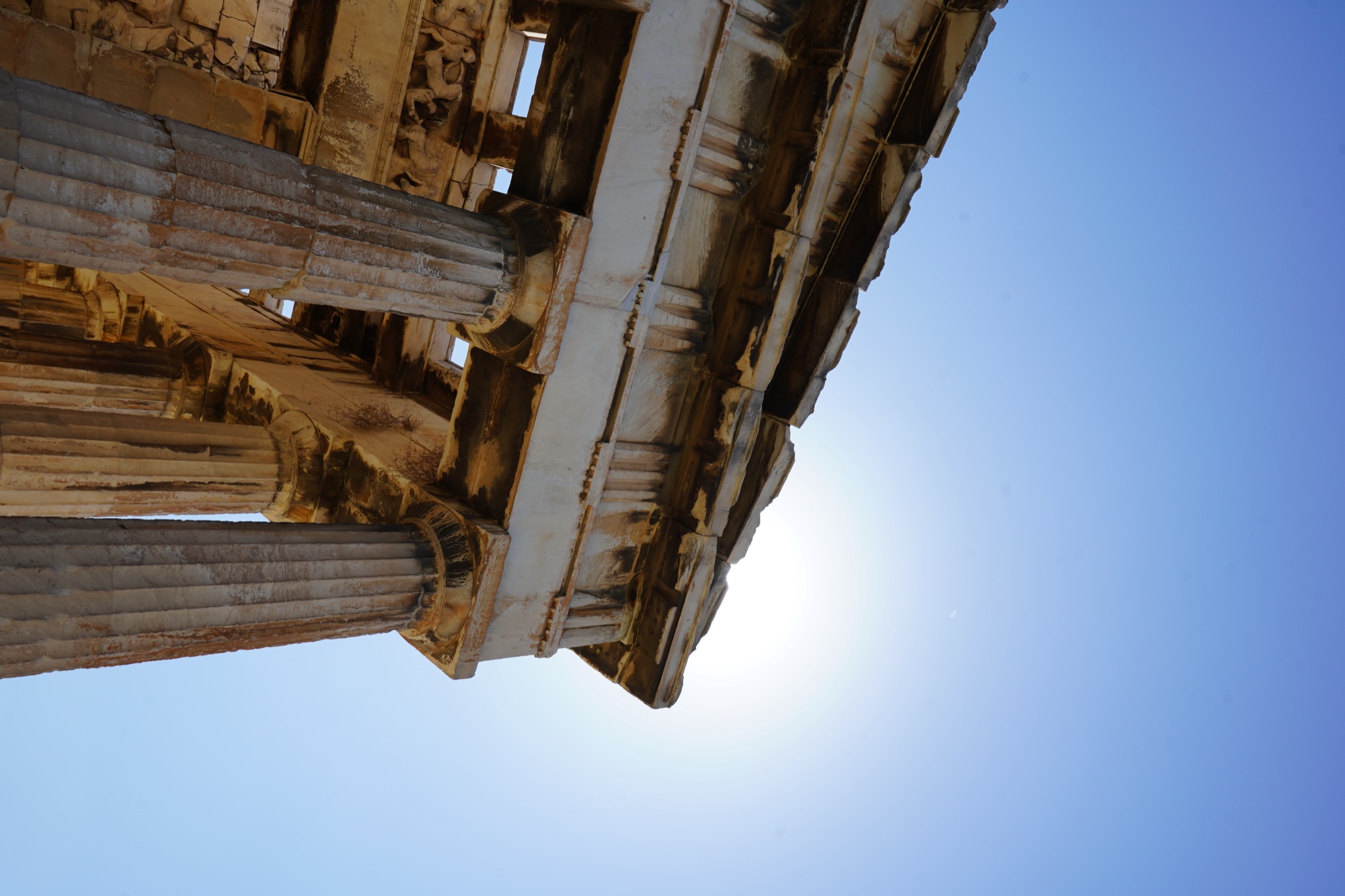 A corner of the Temple of Hephaestus with the sun flaring behind the entablature
