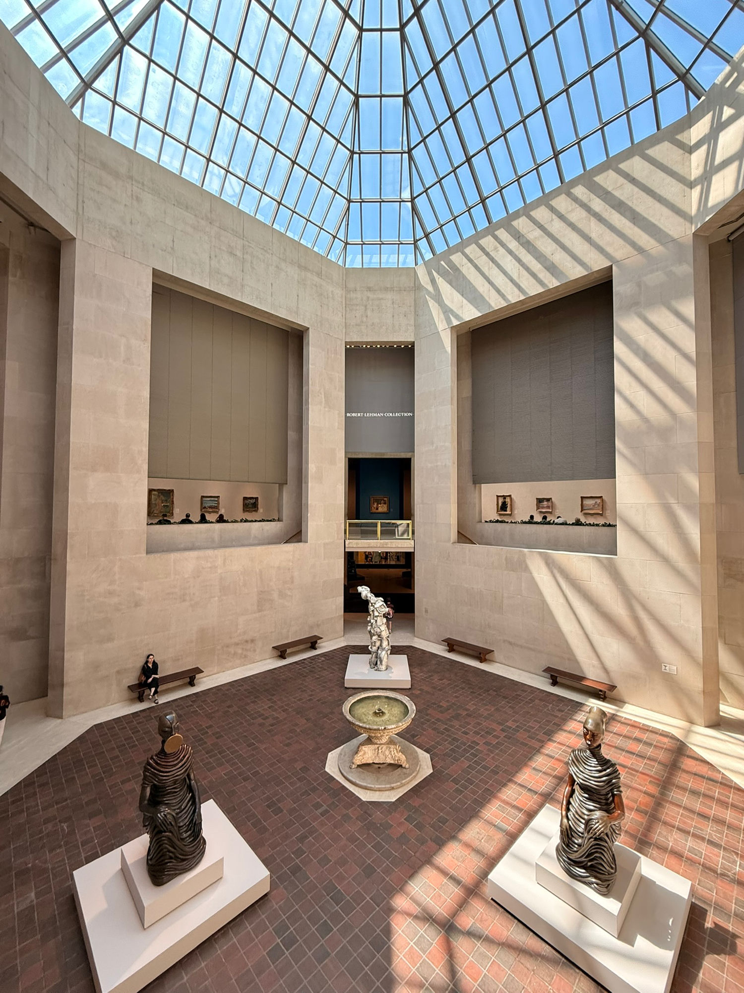 The glass-roofed atrium of the Robert Lehman wing at the Met, sunlight falling in a lattice across stone walls and a brick floor