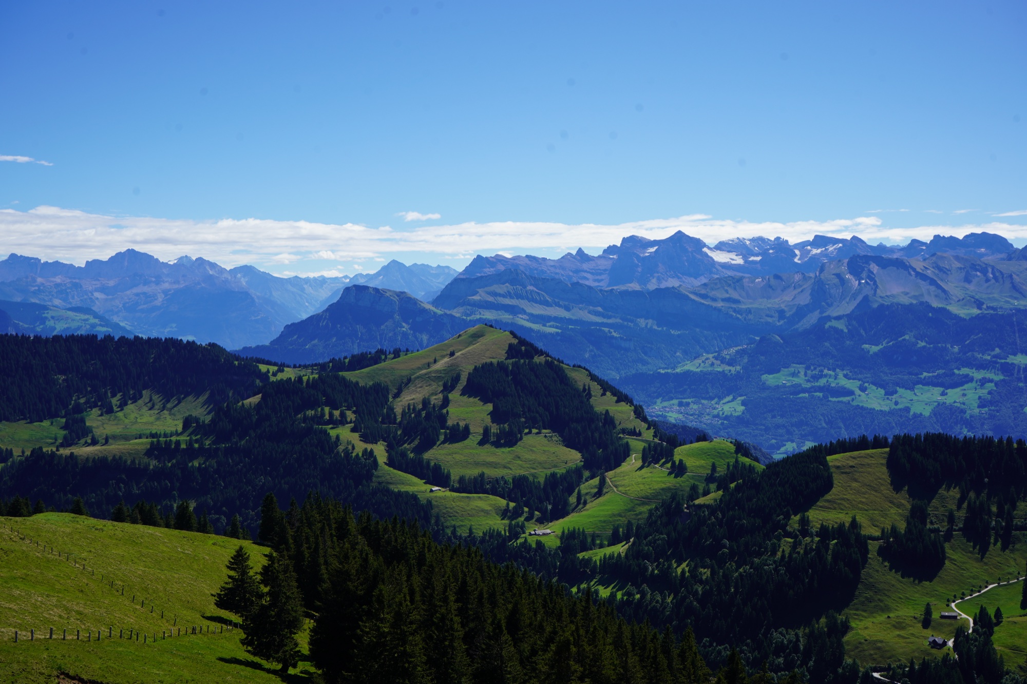 Green pastoral ridges of the Rigi in the foreground, ranks of grey Alps with snow patches behind